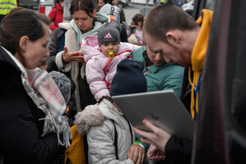 A humanitarian aid worker checks the identities of refugees boarding a bus bound for Portugal outside the main relocation centre in Przemysl, Poland, in March. AFP