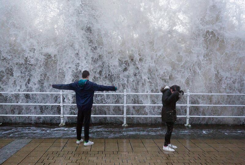 Children stand on the seafront as a wave crashes over the sea wall in Aberystwyth in West Wales. Aaron Chown / PA via AP