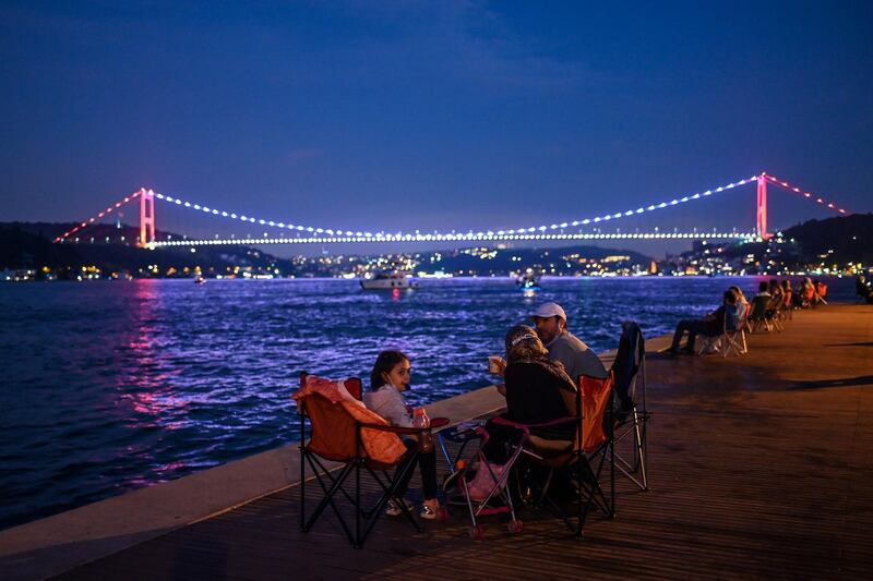 People enjoy the evening as they sit next to the shore of the Bosphorus as Fatih Sultan Mehmet bridge is seen in the backround in Istanbul. AFP