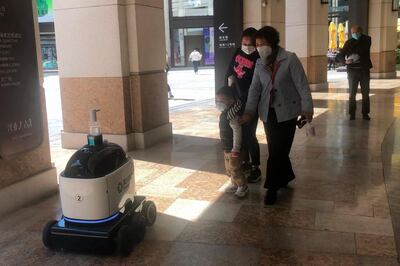 In this March 16, 2020 image made from video, people look at a ZhenRobotics robot as it patrols a plaza in Shanghai. While other industries struggle, one robot maker says China's virus outbreak is boosting demand for his knee-high, bright yellow robots to deliver groceries and patrol malls for shoppers who fail to wear masks. (AP Photo)