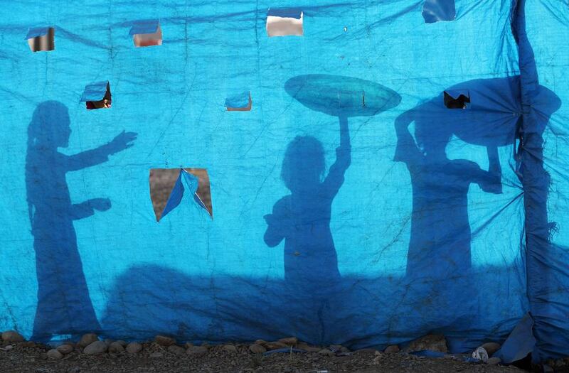 The silhouettes of Iraqi refugee children are seen on tarpaulin as they collect water at the Al Khazir camp located between Erbil and Mosul. Karim Sahib / AFP Photo