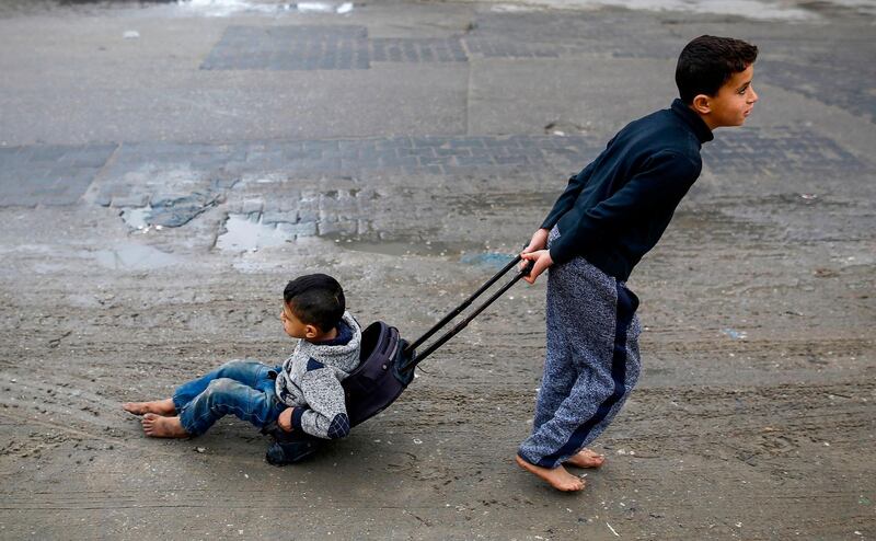 A Palestinian boy pulls his brother as he sits in a wheeled-suitcase as he walks down a street in a refugee camp in Gaza City. Mohammed Abed / AFP