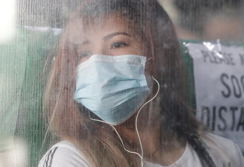 A woman wearing a protective mask looks out from a bus. AP Photo