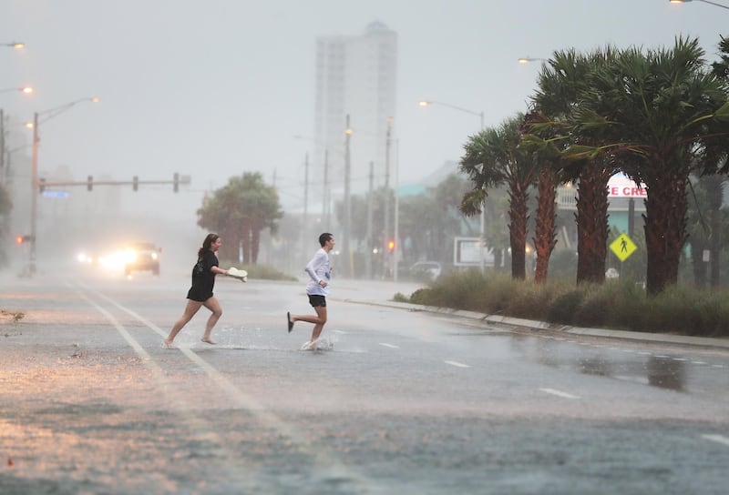 People run across a road through the rain and wind as the outer bands of Hurricane Sally come ashore in Gulf Shores, Alabama. AFP