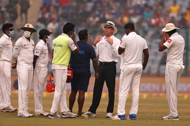 Officiating umpire Nigel Llong, third from right, speaks to Sri Lanka's players, wearing anti-pollution masks, as the game was briefly stopped during the second day of their third test cricket match in New Delhi. Altaf Qadri / AP Photo