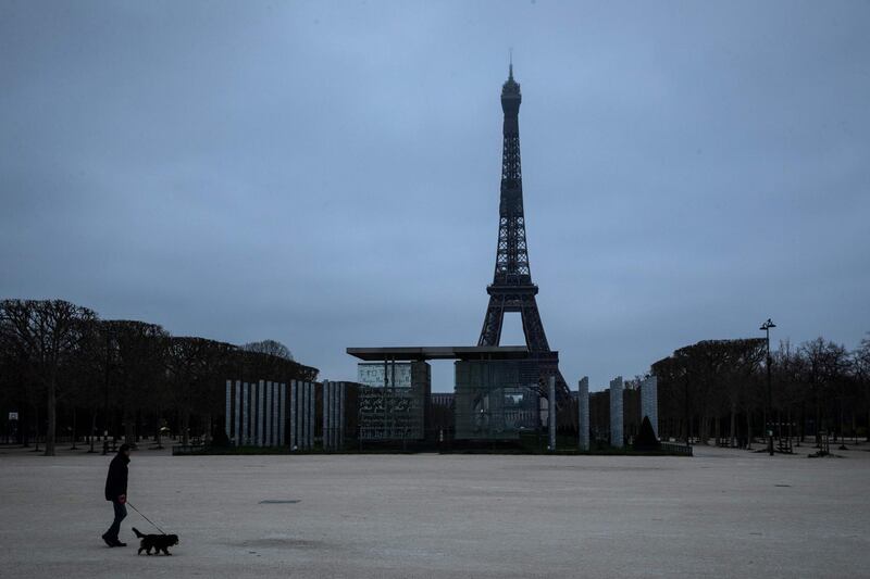 TOPSHOT - A man walks his dog at the Champs de mars on March 21, 2020 in Paris as a strict lockdown comes into in effect in France to stop the spread of COVID-19, caused by the novel coronavirus. A strict lockdown requiring most people in France to remain at home came into effect at midday on March 17, 2020, prohibiting all but essential outings in a bid to curb the coronavirus spread. The government has said tens of thousands of police will be patrolling streets and issuing fines of 135 euros ($150) for people without a written declaration justifying their reasons for being out / AFP / JOEL SAGET
