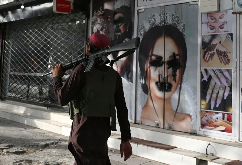 A Taliban fighter walks past a beauty saloon where images of women have been defaced, in Shahr-e Naw neighbourhood in north-west Kabul. AFP