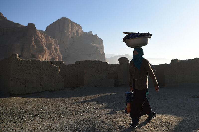 A Hazara woman carries a bucket on her head near the site of the Buddhas of Bamiyan statues, which were destroyed by the Taliban in 2001, in Bamiyan province on March 5, 2021. (Photo by WAKIL KOHSAR / AFP)