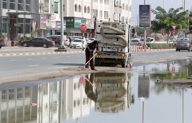 A worker helps clear a road as pools of water remain after recent flooding. 