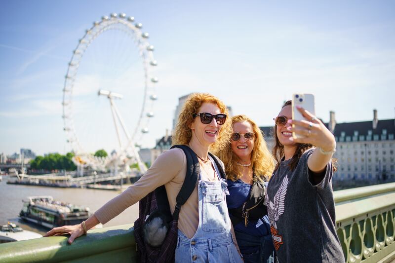 A selfie in front of the London Eye, as people enjoy the sunny weather on Westminster Bridge in London. PA