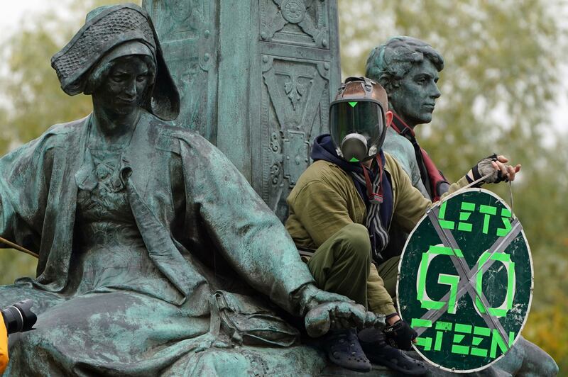 A climate activist climbs a statue during the protest in the centre of Glasgow. AP Photo