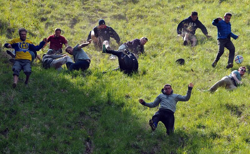 Competitors run down Coopers Hill in pursuit of a fake foam round Double Gloucester cheese during the annual cheese rolling and wake near the village of Brockworth near Gloucester in western England on May 27, 2013. With a disputed history dating back to at least the 1800s, the annual Cooper's Hill Cheese Rolling involves hordes of fearless competitors chasing an eight pound Double Gloucester cheese down a steep hill. The slope has a gradient in places of 1-in-2 and in others 1-in-1, its surface is very rough and uneven and it is almost impossible to remain on foot for the descent. The winner of the race down the hill wins the cheese. AFP PHOTO/CARL COURT
 *** Local Caption ***  209902-01-08.jpg