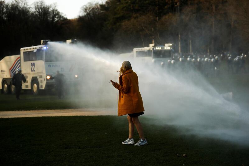 A woman walks as police use a water cannon during clashes in the Bois de la Cambre park in Brussels. Belgian police have clashed with a large crowd in one of Brussels' largest parks, as thousands of revellers had gathered for an unauthorized event despite coronavirus restrictions. AP Photo