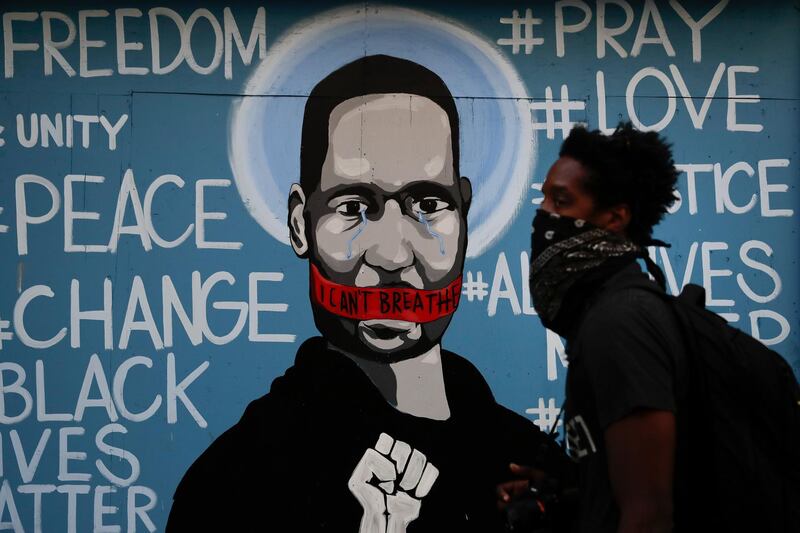 A man with a face covering walks past a mural depicting George Floyd during a protest over the death of Floyd Sunday, May 31, 2020, in Los Angeles. Floyd died in Minneapolis on May 25 after he was pinned at the neck by a police officer. (AP Photo/Jae C. Hong)