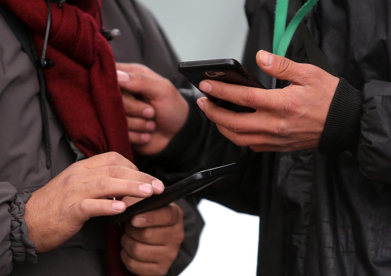 People hold smartphones in their hands while walking outside along a street in the Iranian capital Tehran on November 23, 2019. - Iranians have been struggling to adjust to life offline almost one week into a near-total internet blackout imposed amid violent demonstrations that has forced some to resort to old ways to get by. (Photo by ATTA KENARE / AFP)