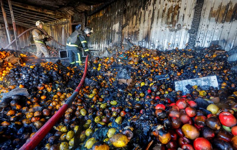 Firefighters stand on heaps of fruit while working inside burnt market stalls in Donetsk, hit by shelling in the course of Russia-Ukraine conflict. Reuters