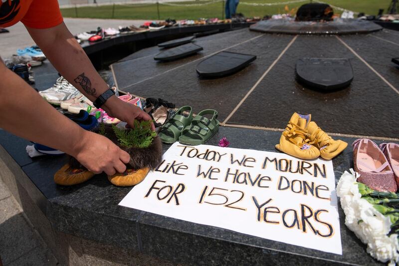 Stephanie Gilpin, whose parents, aunts and uncles were sent to residential schools, smooths out the cedar that she placed in a pair of moccasins at the Centennial Flame on Parliament Hill in Ottawa, Ontario, in memory of the 215 children whose remains were found at the grounds of the former Kamloops Indian Residential School at Tk'emlups te SecwÃ©pemc First Nation in Kamloops, British Columbia, on Sunday, May 30, 2021, (Justin Tang/The Canadian Press via AP)