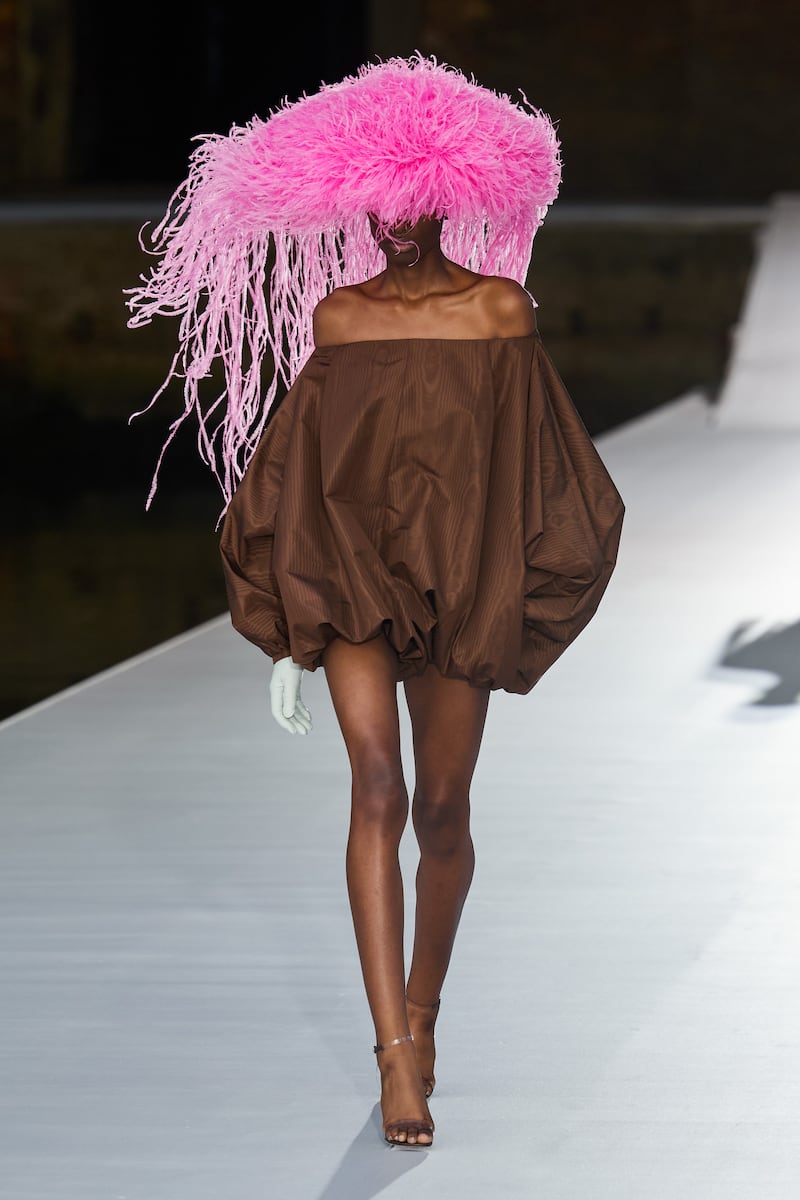 A  micro-puffball-dress in bitter chocolate is worn with a Philip Treacy ostrich feather hat in bright pink at the Valentino autumn 2021 haute couture show