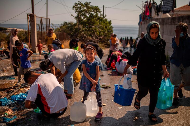 (FILES) In this file photo taken on September 16, 2020 A girl waits to fill bottles with water near a temporary migrant camp on the Greek Aegean island of Lesbos after the Moria camp was destroyed by a fire on the night of September 8.  The failure of the European Union's migration policy could not have been laid out more starkly -- an already miserable camp burned and thousands of refugees homeless. On September 23, 2020, two weeks after the destruction of the Moria camp on the Greek Island of Lesbos, Brussels will launch its latest proposal for EU asylum policy.    / AFP / ANGELOS TZORTZINIS
