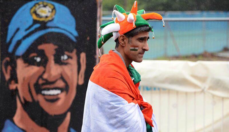 An Indian fan waits in the rain in front of a painting of India's captain Mahendra Singh Dhoni before the ICC Champions Trophy final cricket match against England at Edgbaston cricket ground, Birmingham June 23, 2013. REUTERS/Philip Brown (BRITAIN - Tags: SPORT CRICKET) *** Local Caption ***  PB04_CRICKET-CHAMPI_0623_11.JPG