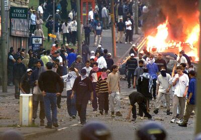Rioters gather in front of police near a burning vehicle in Bradford on the evening of July 7, 2001.  Asian and white youths armed with petrol bombs and baseball bats clashed with police in the industrial city of Bradford on Sunday as northern England suffered a renewed outbreak of race rioting. Reuters