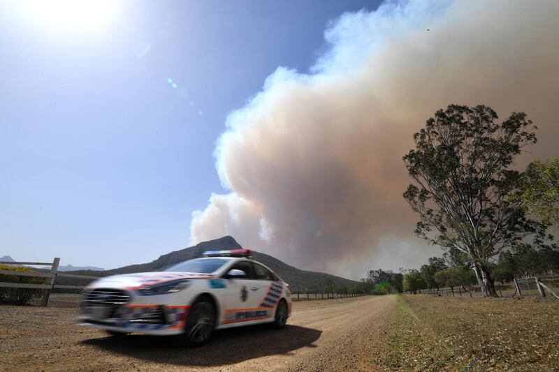 A police vehicle drives away as smoke rises from an out-of-control bushfire near Clumber, Queensland.  EPA