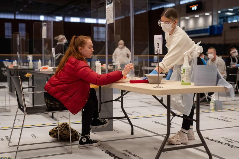 A student places her completed swab into a vial as a member of staff prepares to complete a lateral flow COVID-19 test on it, on the first day of operation of new asymptomatic testing site in the University of Hull's Allam Sport Centre in Hull, northern England on November 30, 2020. The testing site, which has been established through a partnership between the University of Hull and NHS Test and Trace, is aiming to test asymptomatic university students during the first week of December in order to help them return home safely for Christmas. Students will be encouraged to get tested twice during the first week of December using Lateral Flow Devices. If they receive two negative tests they are advised to return home immediately. Should a student test positive they will be required to self-isolate for 10 days, still with enough time to return home for Christmas. / AFP / OLI SCARFF
