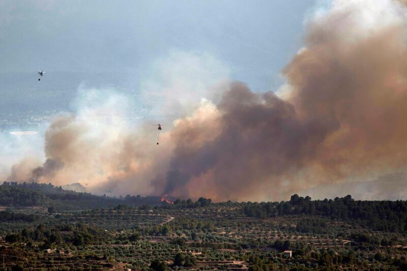 Helicopters continue fighting to extinguish a forest fire as smoke and flames rise in the distance in Bovera. EPA