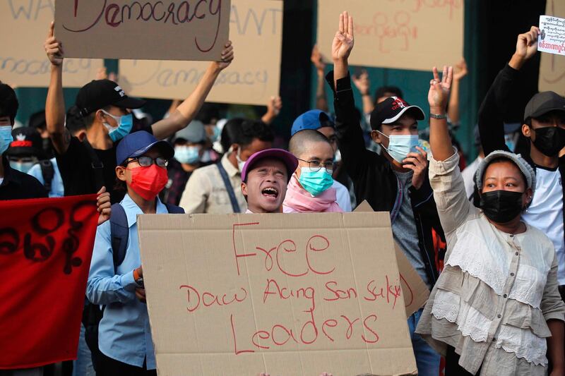 A man shouts while holding a placard while other protesters flash the three-fingered salute  outside the Hledan Center in Yangon, Myanmar. AP