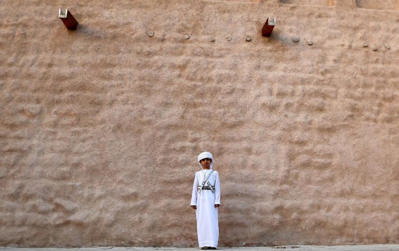 An Emirati boy stands in front of a traditional house.