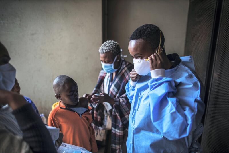 A young boy receives a flue vaccine while a Gauteng Health Department Official adjusts her masks before collecting samples during a door-to-door COVID-19 coronavirus testing drive in Yeoville, Johannesburg, on April 3, 2020. (Photo by MARCO LONGARI / AFP)