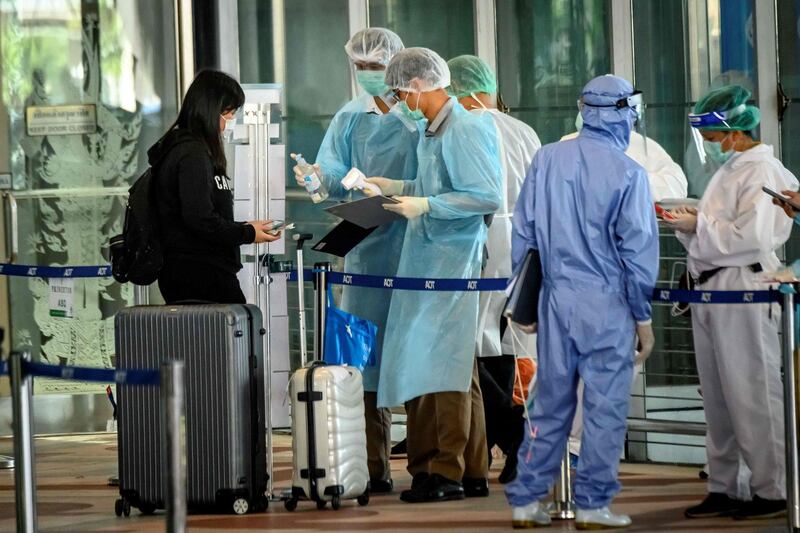 Employees wearing personal protective equipment (PPE) check an arriving international flight passenger before her hotel transfer for the compulsory 14-day Alternative State Quarantine (ASQ), to prevent the spread of the Covid-19 coronavirus, at Suvarnabhumi Airport in Bangkok.   AFP