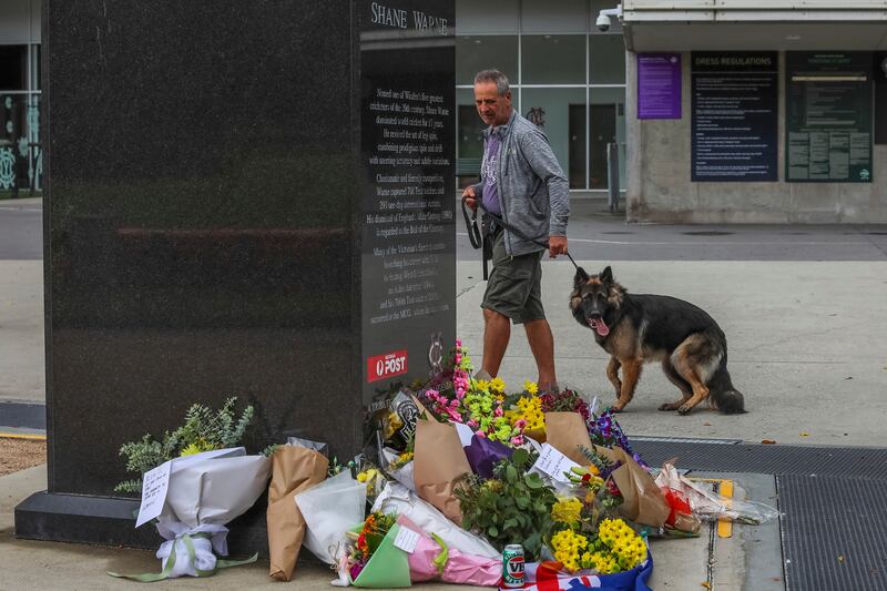A man and his dog view the statue of cricket legend Shane Warne surrounded by flowers outside the Melbourne Cricket Ground. AP