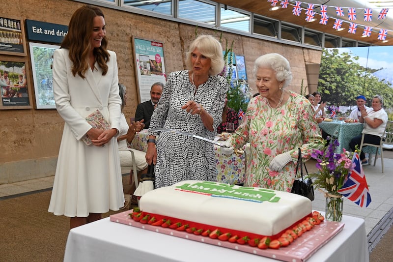 Queen Elizabeth considers cutting a cake with a sword with the Duchess of Cornwall  and Catherine, then Duchess of Cambridge, at The Eden Project, Cornwall, in June 2021