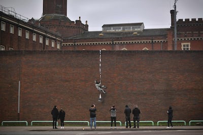 (FILES) In this file photo taken on March 02, 2021 Members of the public pause to look at an artwork by street artist Banksy on the side of Reading Prison in Reading, west of London.  Street artist Banksy on March 4 claimed responsibility for a painting on the wall of a former British prison that once held playwright Oscar Wilde. The artwork shows a prisoner escaping on a rope made of bedsheets tied to a typewriter.
 - RESTRICTED TO EDITORIAL USE - MANDATORY MENTION OF THE ARTIST UPON PUBLICATION - TO ILLUSTRATE THE EVENT AS SPECIFIED IN THE CAPTION
 / AFP / BEN STANSALL / RESTRICTED TO EDITORIAL USE - MANDATORY MENTION OF THE ARTIST UPON PUBLICATION - TO ILLUSTRATE THE EVENT AS SPECIFIED IN THE CAPTION
