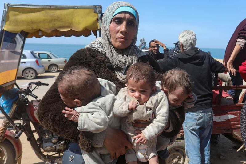A Palestinian woman carries her triplet children as she flees an Israeli raid at Al Shifa Hospital, in Gaza city. Reuters