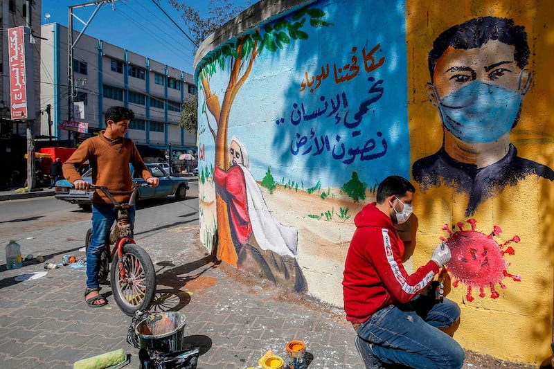 A Palestinian artist paints a mural reading "By fighting the epidemic, we protect the human being and preserve the earth" as a youth watches him in Rafah in the southern Gaza Strip.  AFP