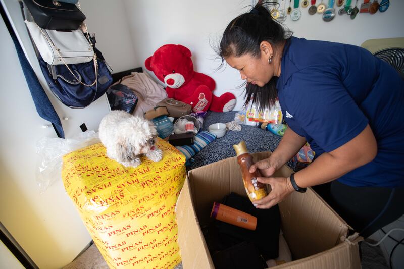 Sharon Toribio, with Max, her employer’s pet, watching on, as she packs Christmas gifts for family in the Philippines. Leslie Pableo for The National
