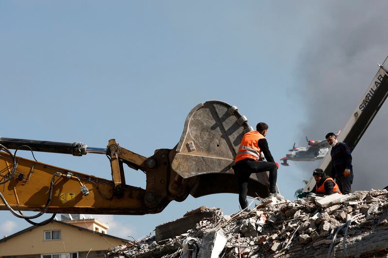 Rescuers rest on top of rubble as an aircraft drops water over a fire at the port in the quake-stricken town of Iskenderun. Reuters