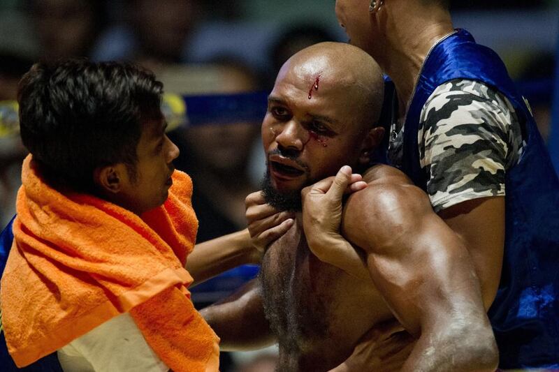 To go with MYANMAR-SPORT-BOXING,FEATURE by Athens Zaw Zaw This photo is taken on December 20, 2015 shows Lethwei martial arts fighter, US national Cyrus "Black Dynamite" Washington (C), reacting following a bloody blow to his face by home champion Tun Tun Min during their bout at the Thein Phyu boxing stadium in Yangon. A roar erupted at the Yangon ring as the home champion ploughed a right hook into his American opponent's face, crumpling him to the canvas in the opening round of the bone-crunching kickboxing bout. With head-butts among the array of painful blows permitted, Lethwei pugilists say their sport is the hardiest member of Southeast Asia's kickboxing family -- even more brutal than Thailand's better known Muay Thai. AFP PHOTO / Ye Aung THU / AFP / Ye Aung Thu