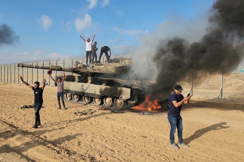 Palestinians with the wreckage of an Israeli tank at the Gaza Strip fence east of the city of Khan Younis on October  7, 2023, the day Hamas forces swept unopposed into Israel. AP Photo