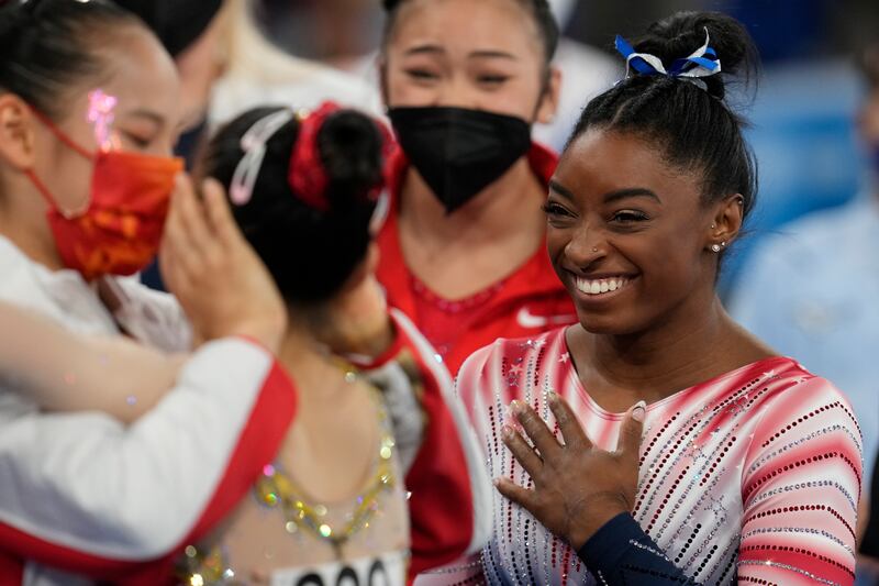 Simone Biles, of the United States, smiles as Tang Xijing, of China, left, embraces teammate Guan Chenchen after the latter won the gold medal on the balance beam during the artistic gymnastics women's apparatus final at the 2020 Summer Olympics.