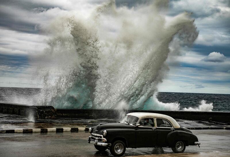 A strong wave crashes into the seawall behind an old American car in Havana, Cuba. AFP