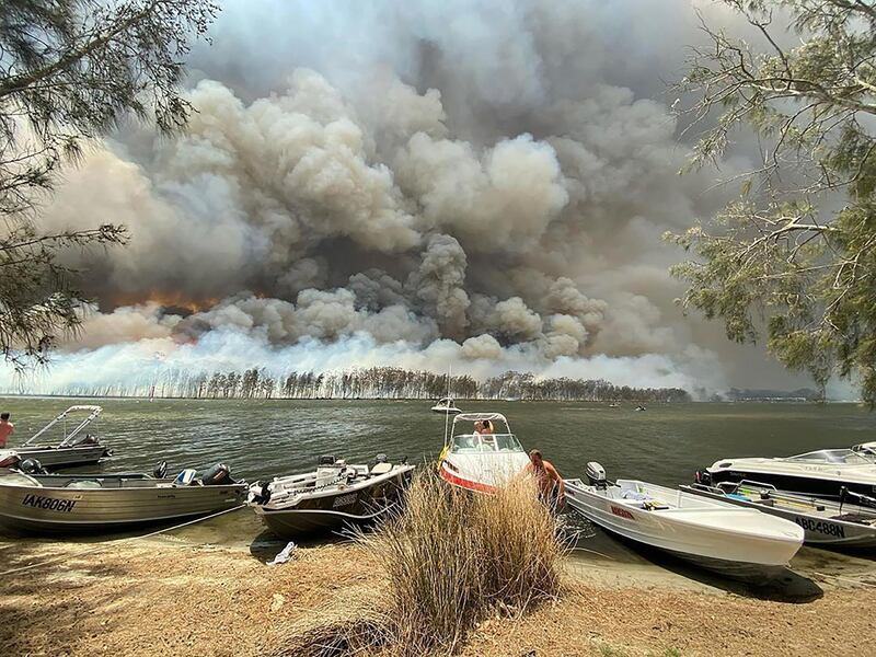 Boats are pulled ashore as smoke and wildfires rage behind Lake Conjola, Australia.  AP