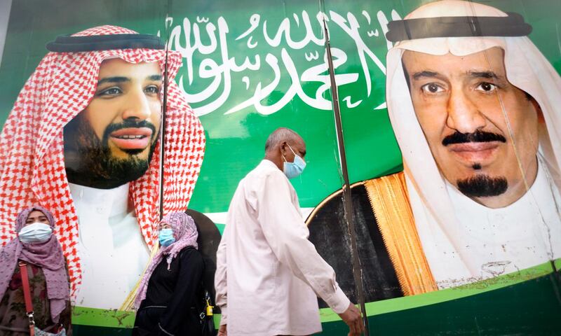 People with face masks walk in front of a banner showing King Salman bin Abdulaziz, right, and Crown Prince Mohammed bin Salman, outside a mall in Jeddah, Saudi Arabia, on February 5. Authorities have re-introduced tough measures to tackle Covid-19. AP Photo