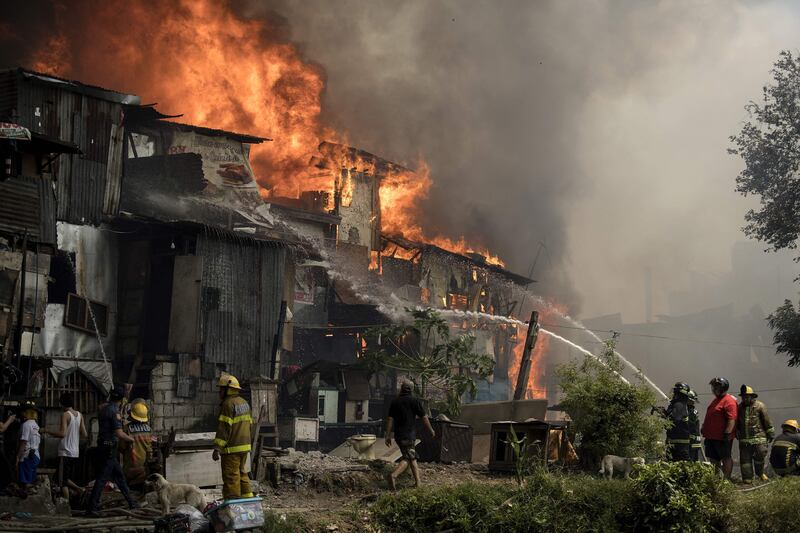 Firefighters extinguish flames as a fire engulfs an informal settlers area beside a river in Manila on August 11, 2017.
Fires are common hazards in the sprawling capital, where millions live in hovels made of scrap wood and cardboard and fire safety regulations are rarely imposed. / AFP PHOTO / NOEL CELIS