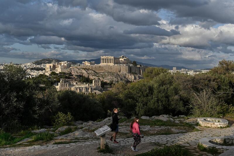 Visitors walk at Filopappou hill, overlooking the Ancient Acropolis in Athens on March 22, 2021. - Greece reopened its open-air archaeological sites on March 22, easing the Covis-19 restrictions as its preparing for opening of tourism season in May. (Photo by Louisa GOULIAMAKI / AFP)