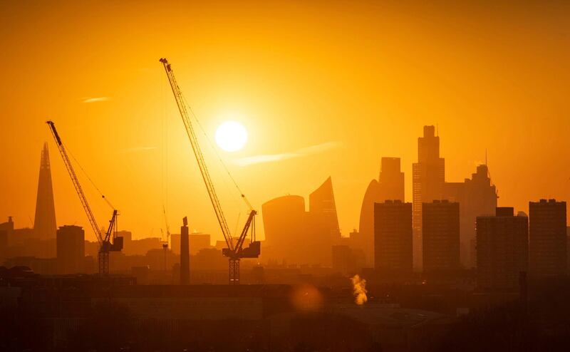 The sun sets behind tower cranes and the London skyline, including the Shard building at left, and other skyscrapers in the city financial district of London, Tuesday Jan. 21, 2020. (Dominic Lipinski/PA via AP)