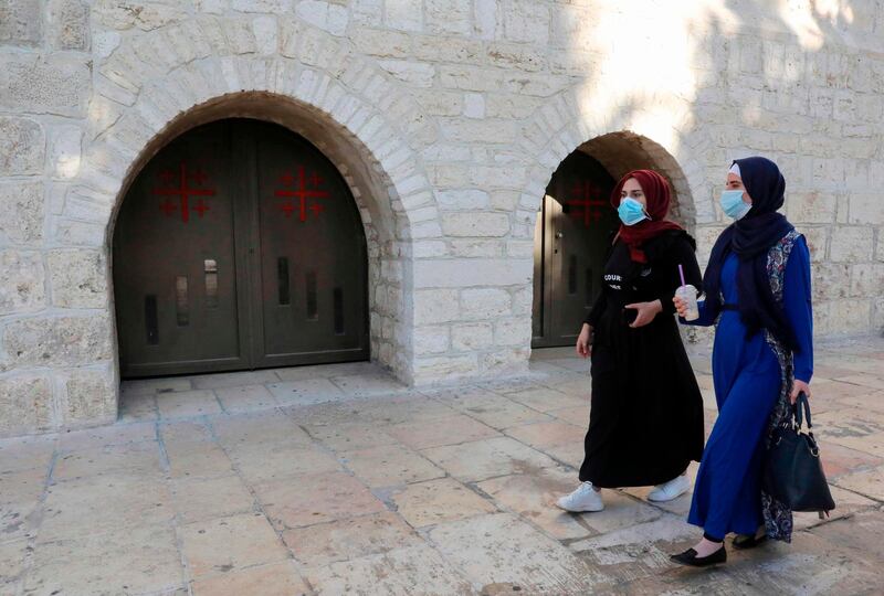 Palestinian women wearing protective masks walk past a closed doorway at the Nativity Church amid lockdown due to the COVID-19 pandemic, in the West Bank city of Bethlehem. AFP