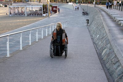 EYHTYW Woman in a wheelchair on a beach access ramp in Barcelona, Spain. PhotoAbility / Alamy Stock Photo